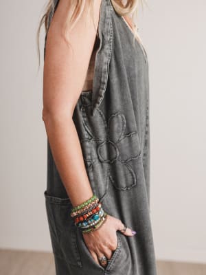 Person wearing a denim dress with floral patterns and colorful bracelets on a neutral background