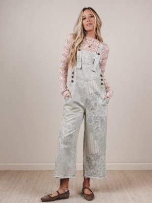 Woman wearing light blue floral overalls with a patterned top against a plain background