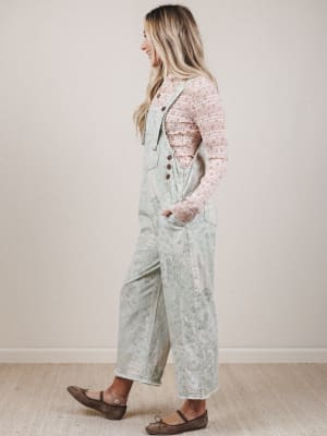Woman wearing light blue overalls with a patterned top against a plain background