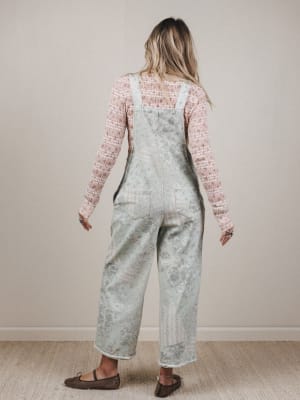 Person wearing a floral overalls and pink long-sleeve shirt against a plain background