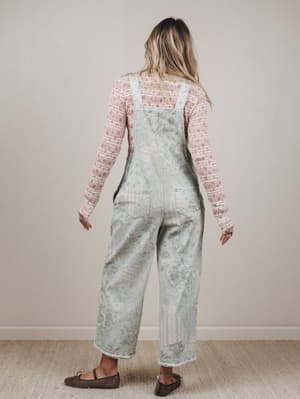 Person wearing a floral overalls and pink long-sleeve shirt against a plain background