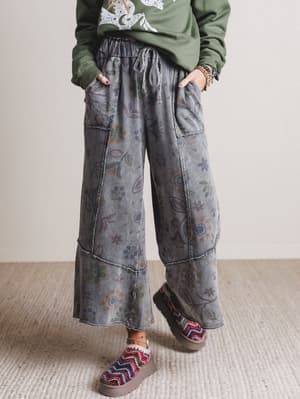 Person wearing floral-patterned wide-leg jeans and a green sweatshirt on a neutral background
