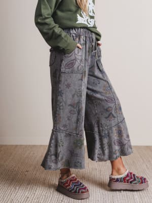 Person wearing patterned gray pants and colorful slippers on a neutral background