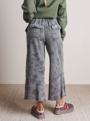 Person wearing floral-patterned pants and a green sweater on a neutral background