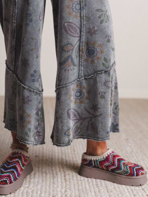 Person wearing colorful sandals and patterned pants on a neutral background