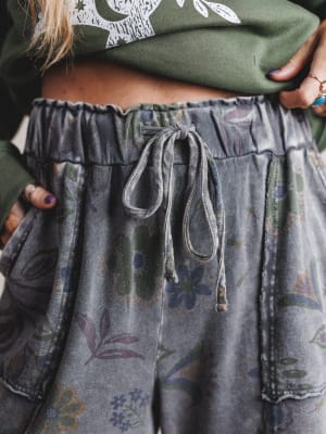 Person wearing a green hoodie and patterned gray pants with a drawstring.