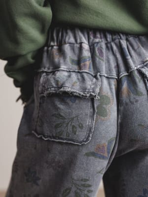 Close-up of a person wearing floral-patterned gray pants with a green sweater.