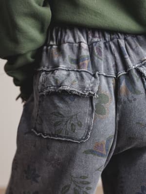 Close-up of a person wearing floral-patterned gray pants with a green sweater.