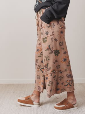 Person wearing a patterned skirt and brown shoes on a neutral background