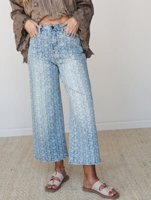 Wide-leg cropped jeans in a soft washed denim with an all-over ditsy floral and pinstripe print, styled with a taupe eyelet blouse, stacked turquoise bracelets, silver rings, and neutral buckle sandals — the kind of outfit that looks effortless but w