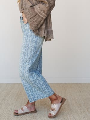 A side-profile shot of floral-striped wide-leg jeans paired with a mocha eyelet bell-sleeve top and neutral buckle sandals — the kind of outfit that looks like it came together effortlessly but you definitely planned it.