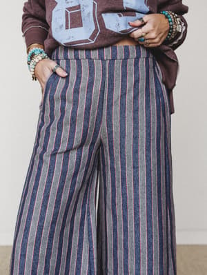 A mid-shot focused on wide-leg striped pants in navy, grey, and red paired with a mauve graphic sweatshirt — the kind of effortless, collected outfit that makes casual feel completely intentional.