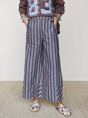 Wide-leg striped pants with a chevron hem detail styled casually with a graphic sweatshirt, stacked boho bracelets, and cow-print slip-ons — the kind of outfit that looks thrown together in the best possible way.