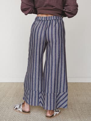 Back view of wide-leg striped pants in navy, grey, and red paired with a cropped burgundy sweatshirt and cow-print slides — relaxed and a little retro in the best way.