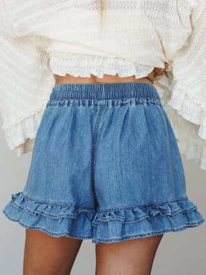 Flowy washed denim shorts with double ruffle hem and an elastic waistband, styled with a cream crochet crop top — the kind of outfit that feels equally at home at a farmers market or a rooftop happy hour.