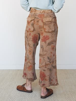A back-view shot of wide-leg cropped pants in a warm mocha waffle knit with an all-over floral print, styled with a light blue sweatshirt and suede clogs — the kind of pants that feel like they were made from a vintage tapestry in the best way.