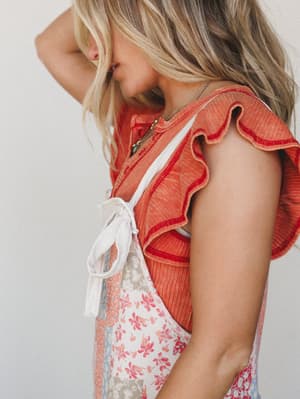 A close-up side profile shot of a ruffled terracotta crop top layered over a floral patchwork jumpsuit, styled with a delicate turquoise pendant necklace — warm, feminine, and effortlessly boho.