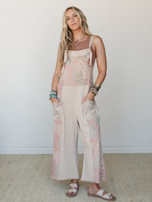 A wide-leg patchwork jumpsuit in soft khaki and blush tones, styled with a layered tank underneath, stacked bracelets, and white sandals — the kind of outfit that looks effortless but clearly wasn't an accident.