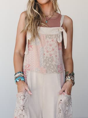 A sun-kissed close-up of a patchwork floral jumpsuit layered over a dusty rose tank, styled with stacked turquoise and beaded bracelets — the kind of outfit that looks like it's been loved for years.