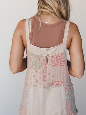 A back-view shot of a patchwork floral jumpsuit layered over a mauve ribbed tank, showing off the button keyhole back detail and a delicate gold chain necklace — the kind of outfit that looks like it was thrifted perfectly.