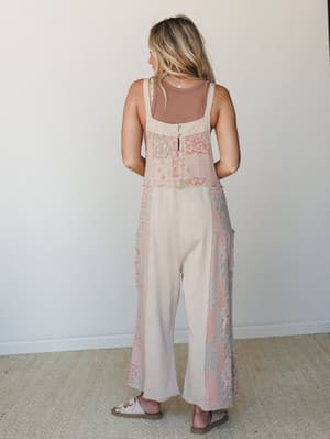 A back-view shot of a wide-leg patchwork jumpsuit in soft khaki with floral print panels, layered over a mauve ribbed tank — relaxed, earthy, and effortlessly lived-in.