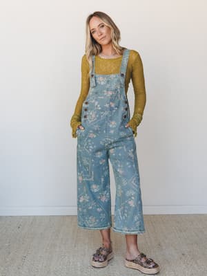 A floral-printed denim overall styled over a mossy green lace long-sleeve — the kind of outfit that looks like it wandered out of a vintage shop and into something better.