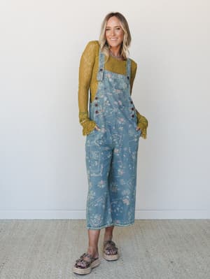 A wide-leg floral denim overall worn over a moss green lace long-sleeve top, styled with platform espadrille sandals — the kind of outfit that looks effortless but is clearly very intentional.