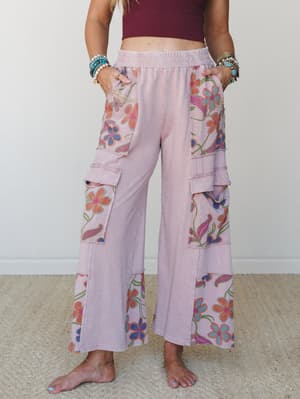 Wide-leg cargo pants in washed mauve with bold floral patchwork panels bring a retro-garden energy — the kind of pants that make errands feel like a personality.