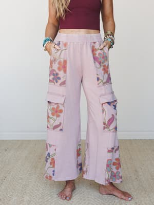 Wide-leg cargo pants in washed mauve with bold floral patchwork panels at the pockets and hem, styled with a cropped burgundy top and stacked boho bracelets — the kind of pants that do all the talking.