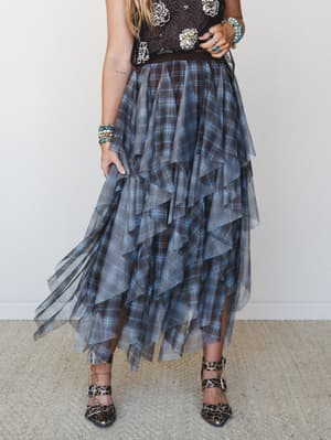 A tiered plaid maxi skirt with a sheer tulle overlay cascades in dramatic ruffled layers, styled with a dark embellished top, stacked turquoise bracelets, and leopard print heels for an unexpectedly cool mix of textures.
