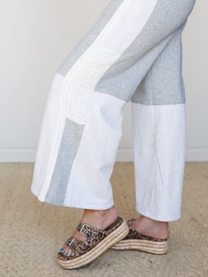 A close-up detail shot of wide-leg pants in heather grey with colorblock paneling and lace trim inserts, styled with leopard print espadrille platform sandals for an unexpected, personality-forward pairing.
