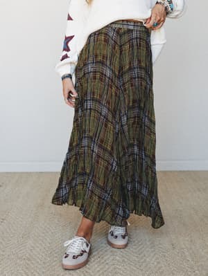 An olive and brown plaid maxi skirt styled with a cream star-print sweater and casual sneakers — the kind of effortless fall outfit that looks like it came together on accident but absolutely didn't.