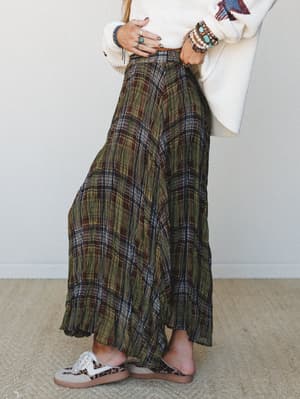 A flowy plaid maxi skirt in olive and brown pairs with a cream knit sweater and leopard slides — the kind of outfit that looks like it came together effortlessly but absolutely did not.