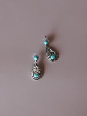 A pair of silver teardrop drop earrings with turquoise stone cabochons and intricate filigree detailing, laid against a soft dusty mauve background — the kind of earrings that feel equally at home on a Tuesday or a road trip.