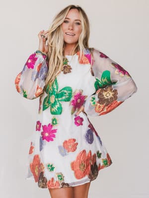 Woman wearing a colorful floral dress with sheer sleeves on a plain background