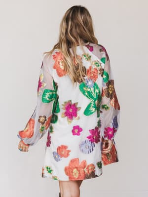 Woman wearing a colorful floral dress with a sheer overlay on a plain background