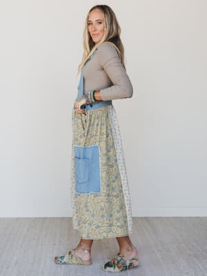 Woman wearing a floral dress with blue patchwork overalls against a white background