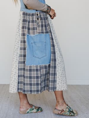 Person wearing a patchwork skirt with plaid and denim patterns on a plain background