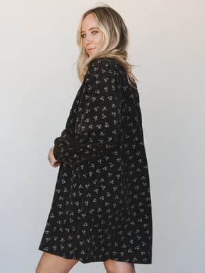 A flowy black mini dress in what looks like a velvet or corduroy fabric, scattered with tiny ditsy florals — the kind of dress that works just as hard at a holiday party as it does at a Sunday brunch.