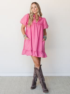 A bright orchid pink mini dress with puff sleeves and ruffle hem styled with dark brown cowboy boots and stacked turquoise bracelets — playful and a little Western, the kind of outfit that works just as hard at a concert as it does at brunch.