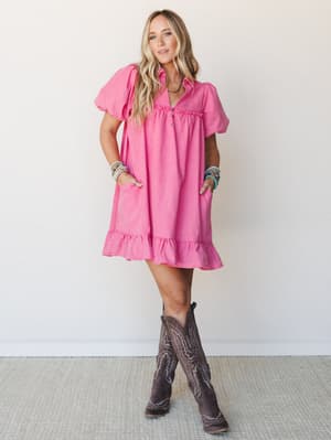 A bright orchid pink mini dress with puff sleeves and ruffle hem styled with dark brown cowboy boots and stacked turquoise bracelets — playful and a little Western, the kind of outfit that works just as hard at a concert as it does at brunch.