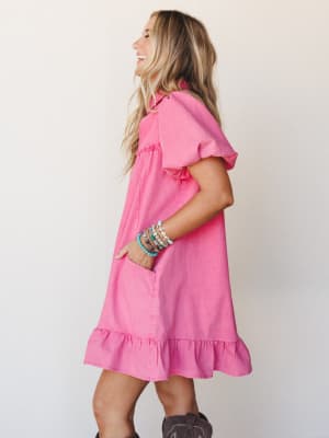 A bright hot pink mini dress with flutter sleeves and a ruffle hem worn with western boots and a stack of colorful beaded bracelets — the kind of outfit that makes a Tuesday feel like something worth showing up for.