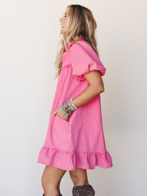 A bright hot pink mini dress with flutter sleeves and a ruffle hem worn with western boots and a stack of colorful beaded bracelets — the kind of outfit that makes a Tuesday feel like something worth showing up for.
