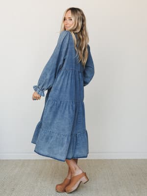 A denim maxi dress with effortless boho energy — tiered skirt, billowy long sleeves with ruffle cuffs, and a washed finish that feels worn-in and personal, styled with wood-heel clogs for a free-spirited everyday look.