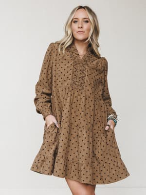 A camel-toned corduroy mini dress with a polka dot print, ruffle placket neckline, and tiered skirt — the kind of dress that feels like fall wrapped around you, styled with stacked turquoise bracelets for a little boho warmth.