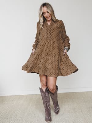 A tiered mini dress in warm mocha with a polka dot print, styled with tall cowboy boots and stacked turquoise bracelets — the kind of outfit that feels equally at home at a fall farmers market or a weekend brunch.