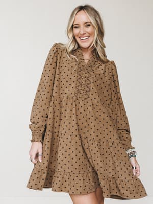 A smiling model wears a mocha corduroy polka dot mini dress with a relaxed, flowy silhouette — the kind of dress that feels equally at home at a fall farmers market or a Sunday brunch.