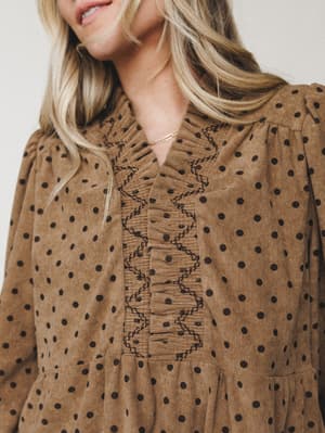 A close-up detail shot of a mocha corduroy dress with polka dots, highlighting the intricate embroidered ruffle placket and tiered bodice — the kind of piece that feels like autumn in the best possible way.