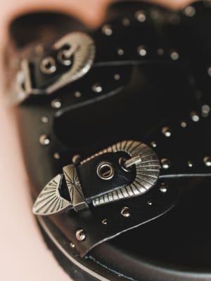 Close-up of a black leather belt with silver metal buckle and decorative elements.
