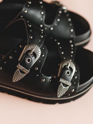 Black leather shoes with decorative metal accents on a pink background